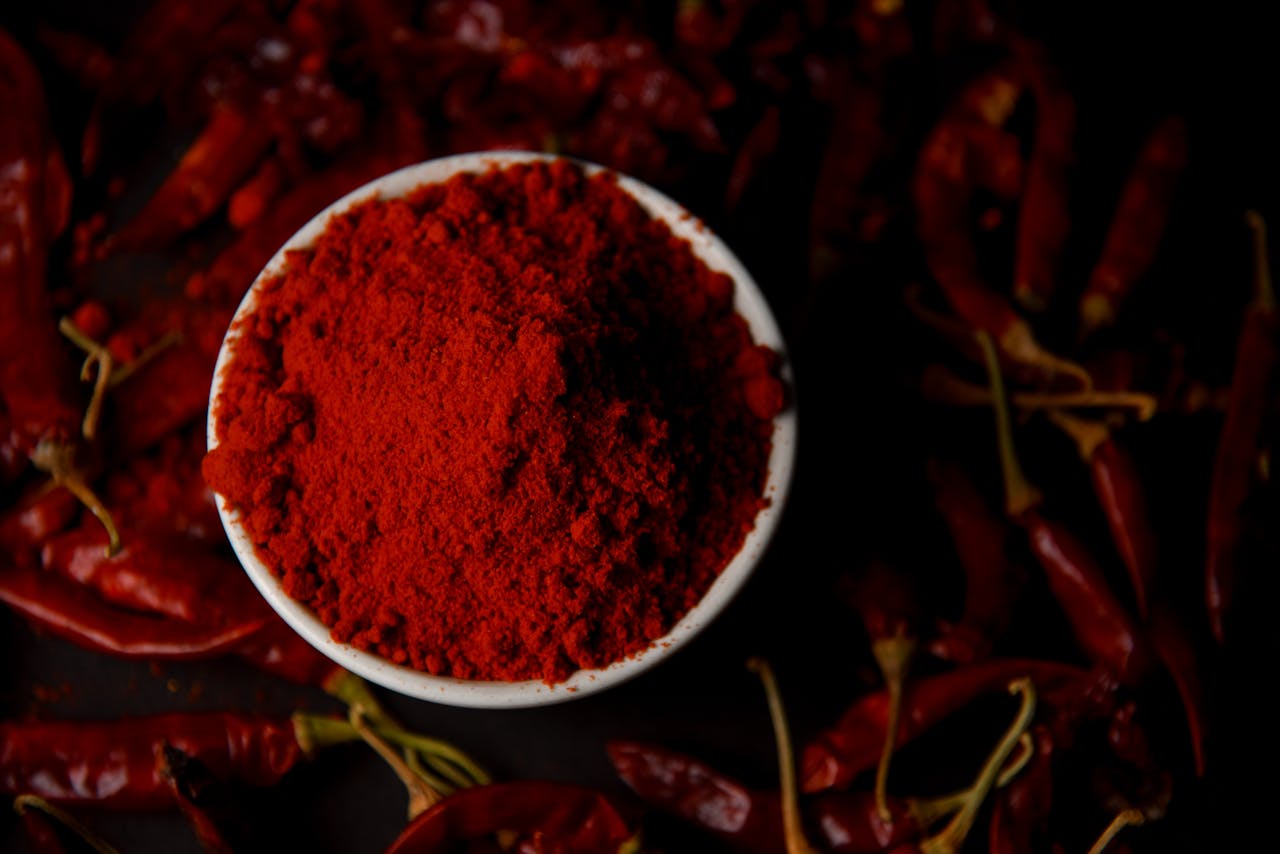Vibrant chili powder in a bowl surrounded by dried red chilies, perfect for spice lovers.